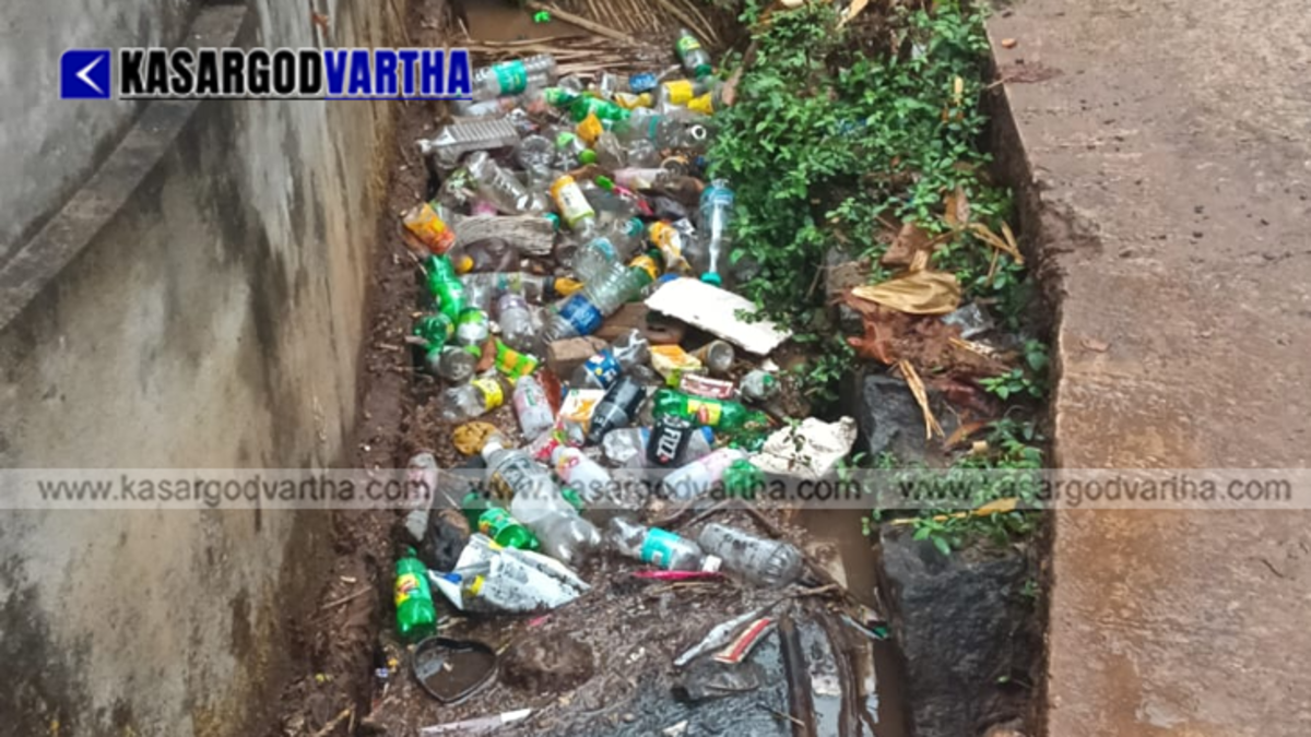 A completely blocked town drainage canal in Kasaragod filled with mud and floating plastic waste bottles during rain.