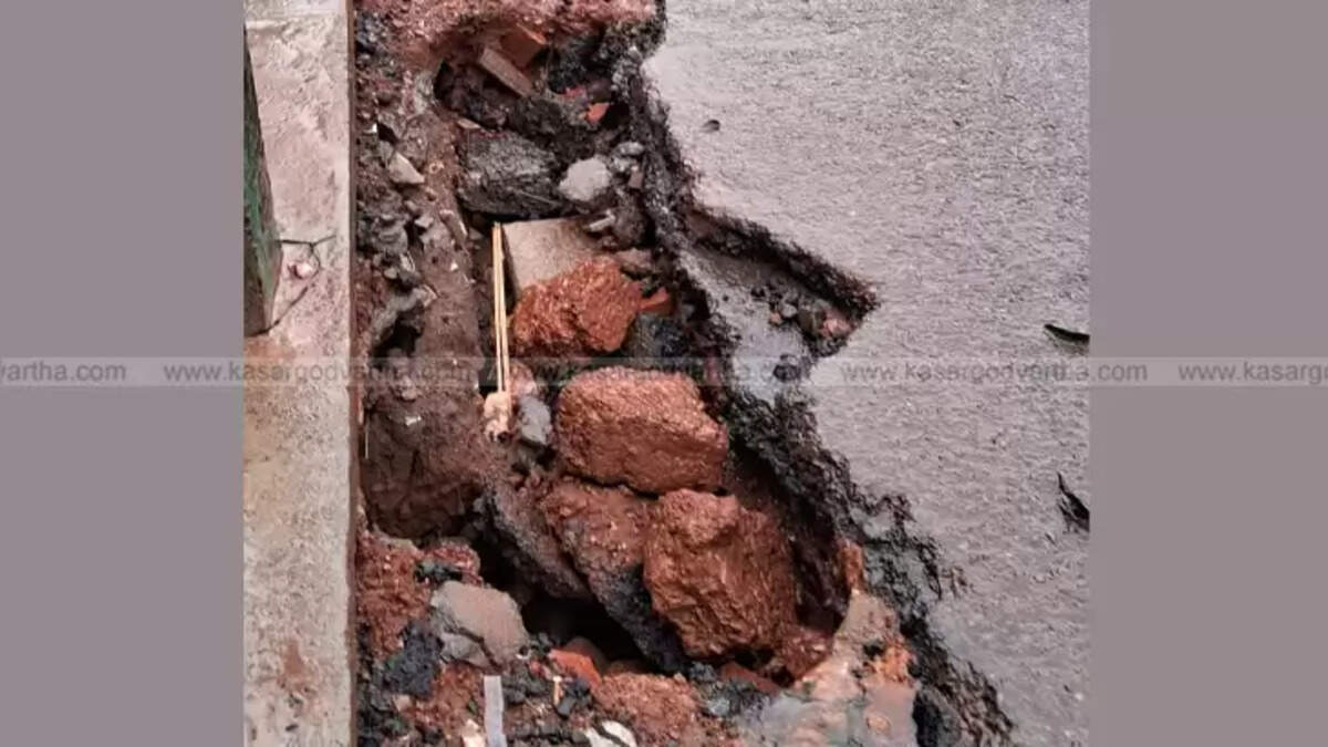 A damaged road in Kasaragod city after heavy rains, showing potholes and exposed gravel.
