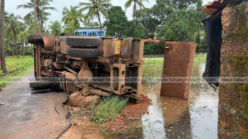 A tipper lorry overturned in a pit on the side of a road in Trikaripur.