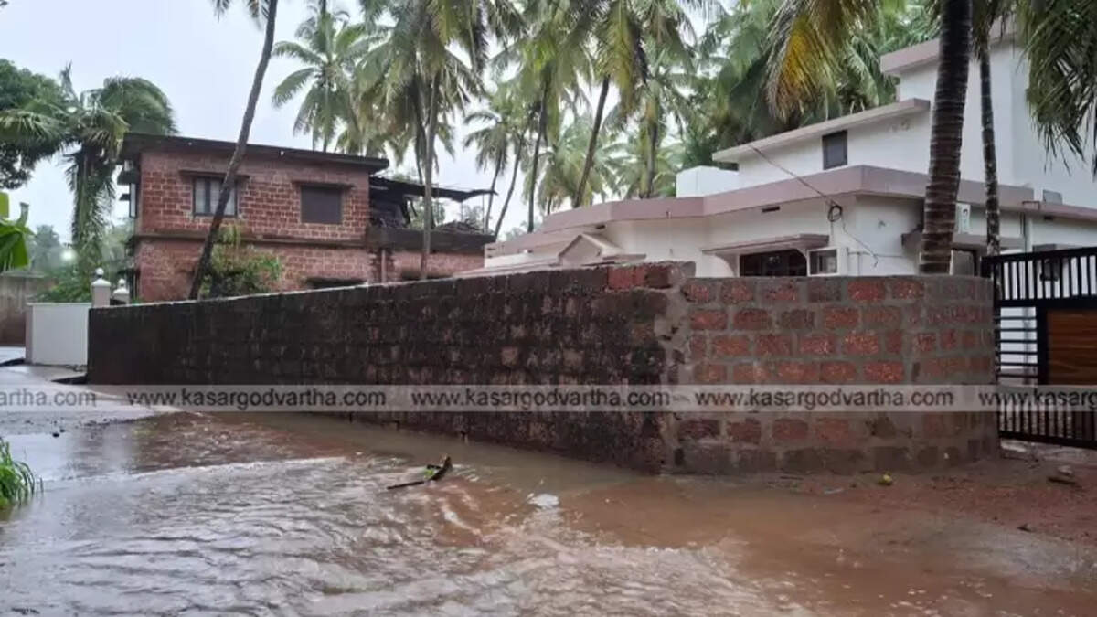 Waterlogged street in Uppala, Kasaragod, with submerged vehicles and homes.