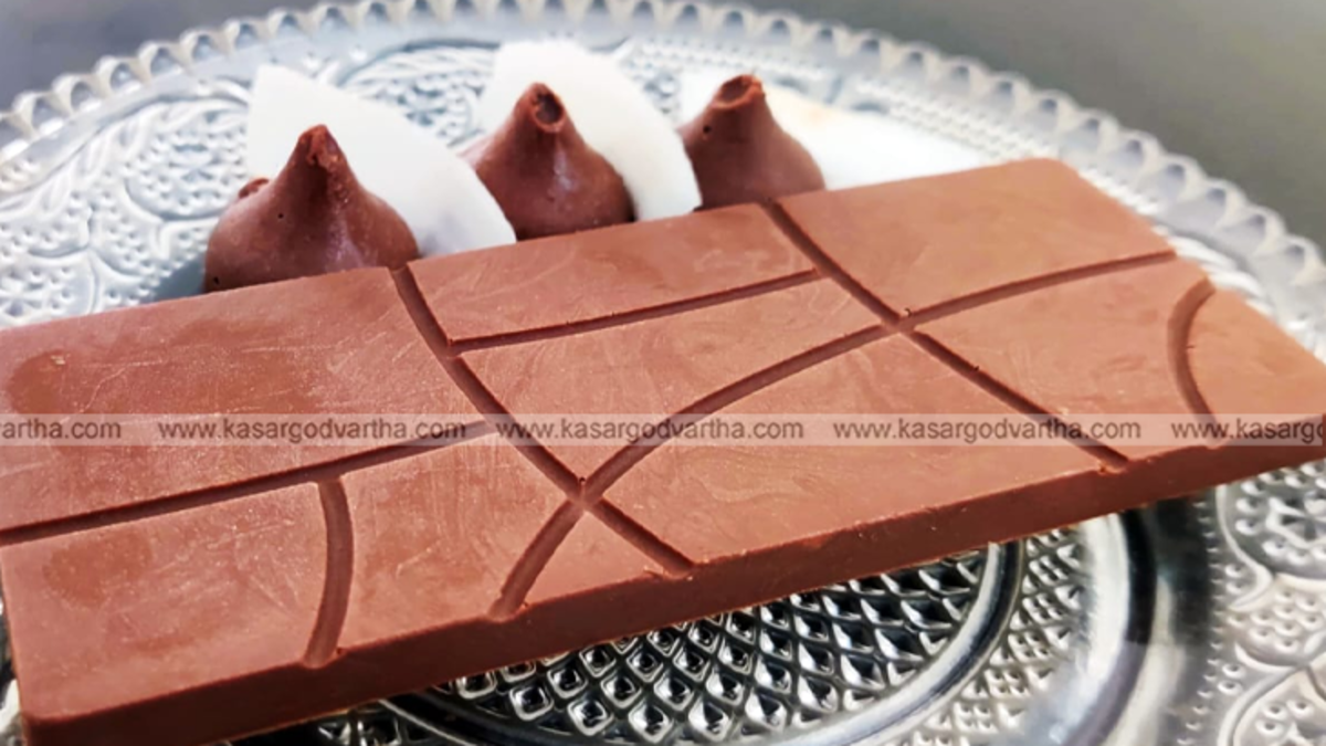 Close-up of a milk chocolate bar with geometric line patterns on a decorative glass plate, featuring chocolate truffles and coconut slices in the background.
